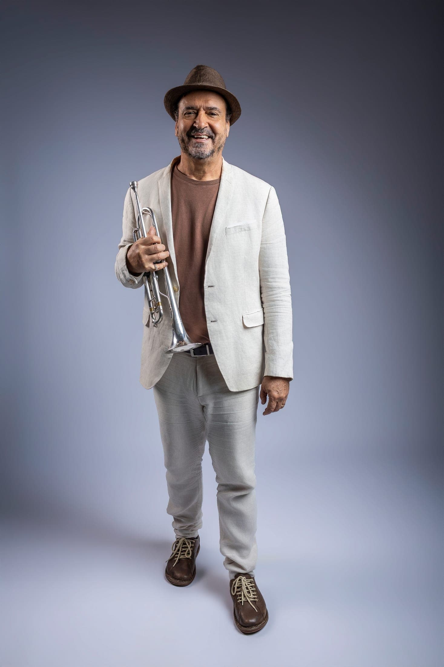 Full-length portrait of Silvério Pontes in a light linen suit and hat, smiling, trumpet in hand